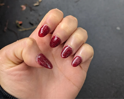 Hand with red glittery nail polish on a dark background